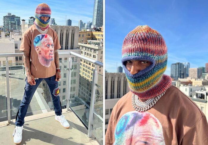 Person embracing fashion risks with colorful knit balaclava and graphic shirt, standing on a rooftop with city skyline.