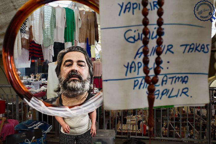 Street scene with unique reflections, showcasing garments and signs, embodying Gökhan Arer's distinct photographic perspective.