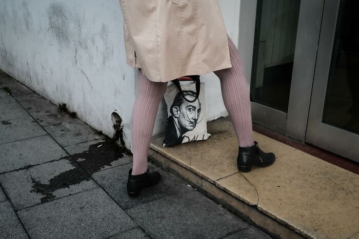 Person in pink tights and black shoes carries a bag with artwork, showing Gökhan Arer's unique street photography.