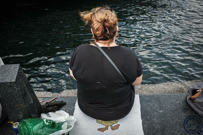 Person sitting by the water, captured with unique perspective, items placed nearby.