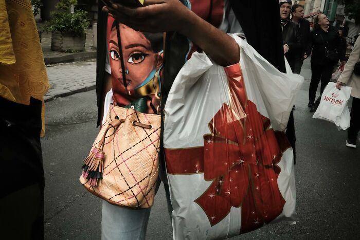 Street photo with a woman holding a bag featuring a cartoon face, demonstrating Gökhan Arer's unique perspective.
