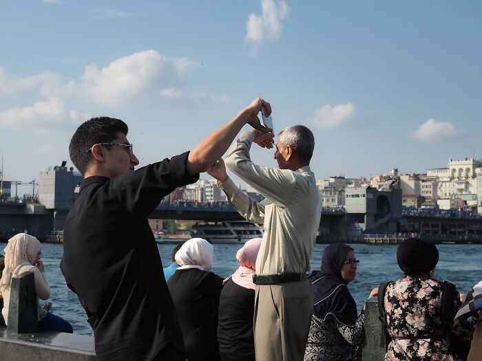 People enjoying a riverside view, with two men creatively posing, showcasing unique street photography skills.