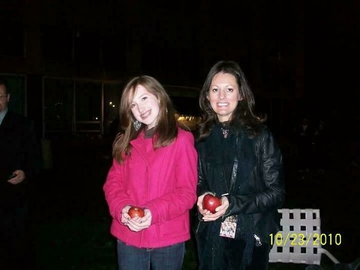 Two women holding apples, smiling at night outdoors, a nostalgic moment capturing people’s regrettable past photos.