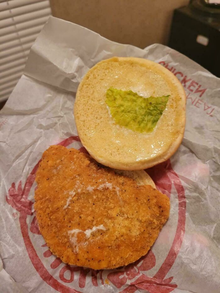 Chicken sandwich with a single lettuce patch, illustrating food service compliance with customer requests for extras.