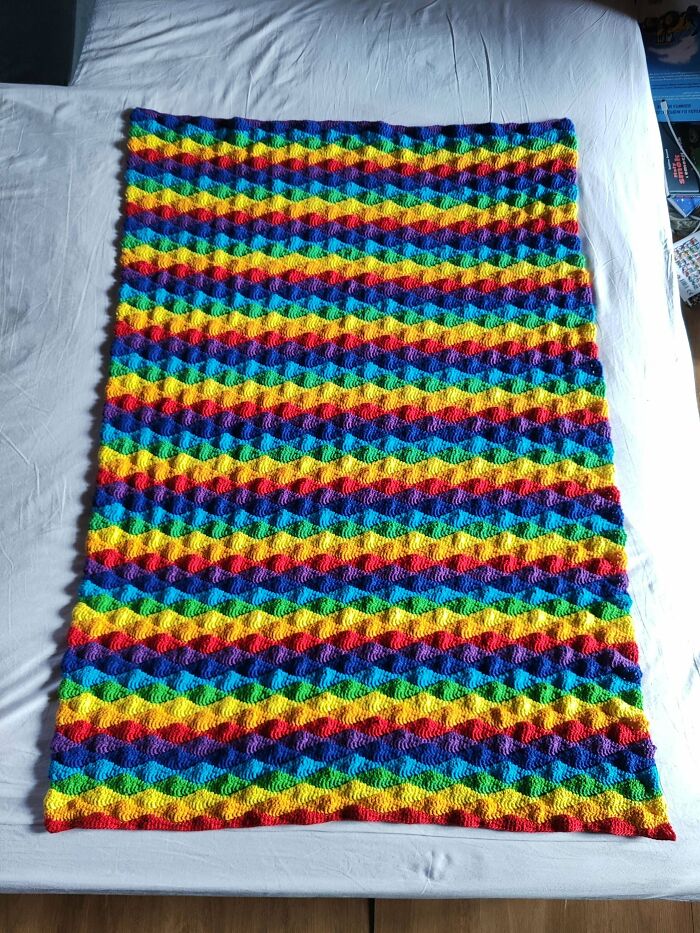 Colorful crocheted blanket with vibrant diagonal stripes showcasing crochet masterpieces and patterns on a white surface.
