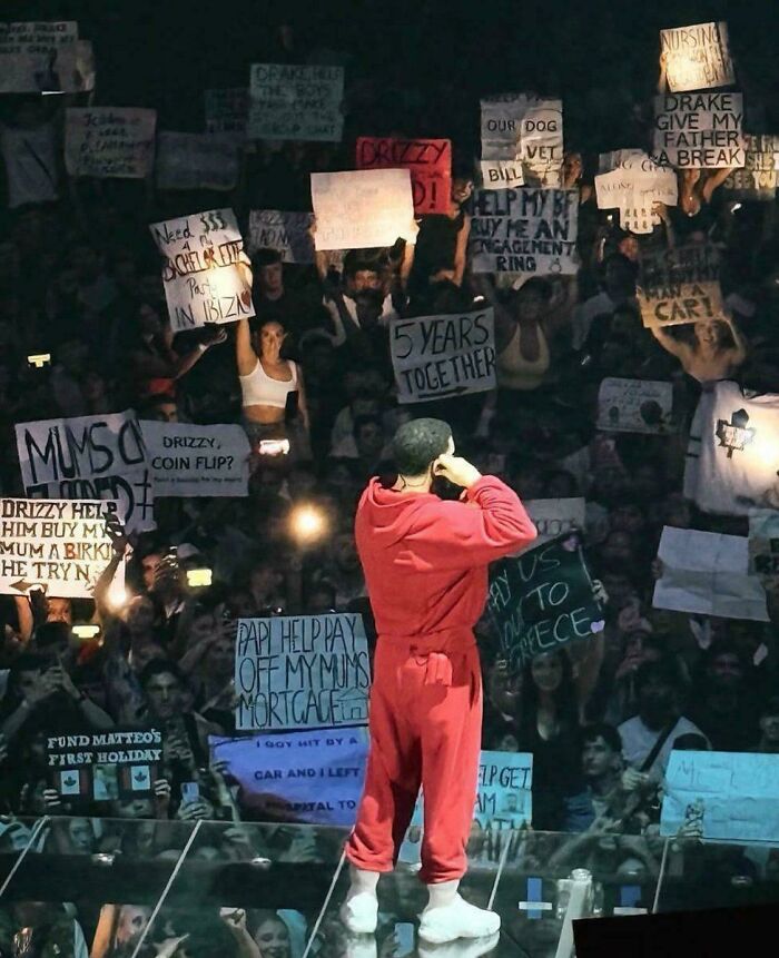 Performer in a red outfit facing a crowd holding various signs, capturing a moment of modern life and its boring dystopia.