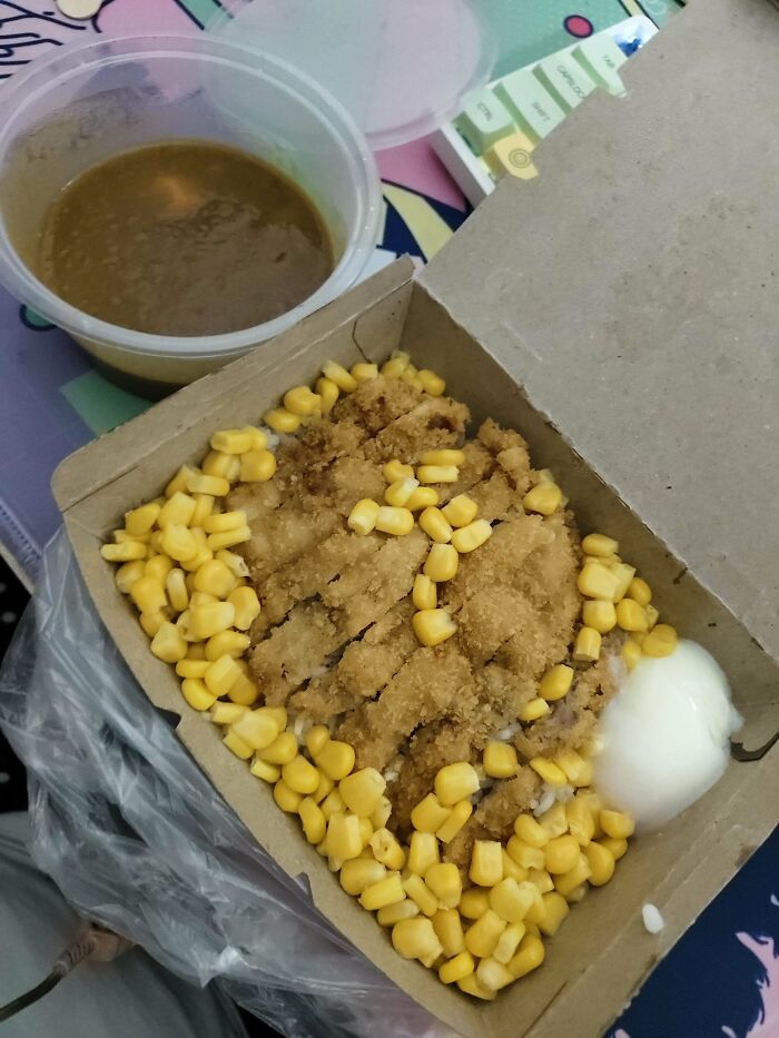 Extra corn and sauce on breaded dish in takeout box, showcasing delicious compliance by food service workers.