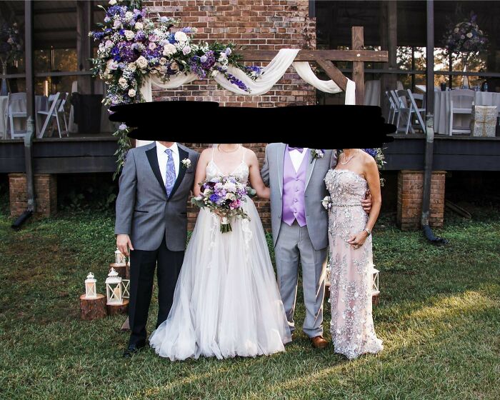 Wedding party photo with faces obscured, featuring people in formal attire and a floral archway backdrop.