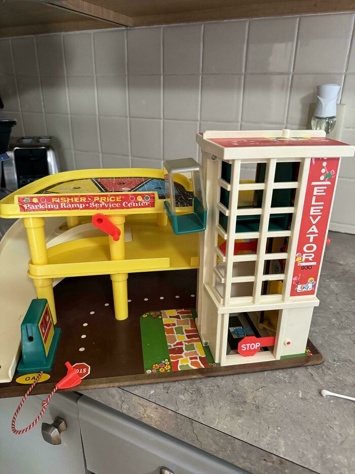 Vintage toy parking garage with elevator, featuring a Fisher-Price design, sitting on a gray countertop.