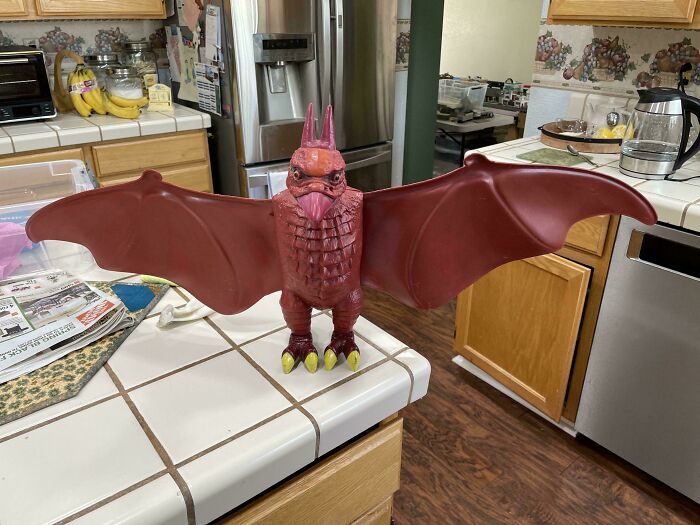 Vintage toy of a red creature with wings, standing on a kitchen counter with tiled surface.