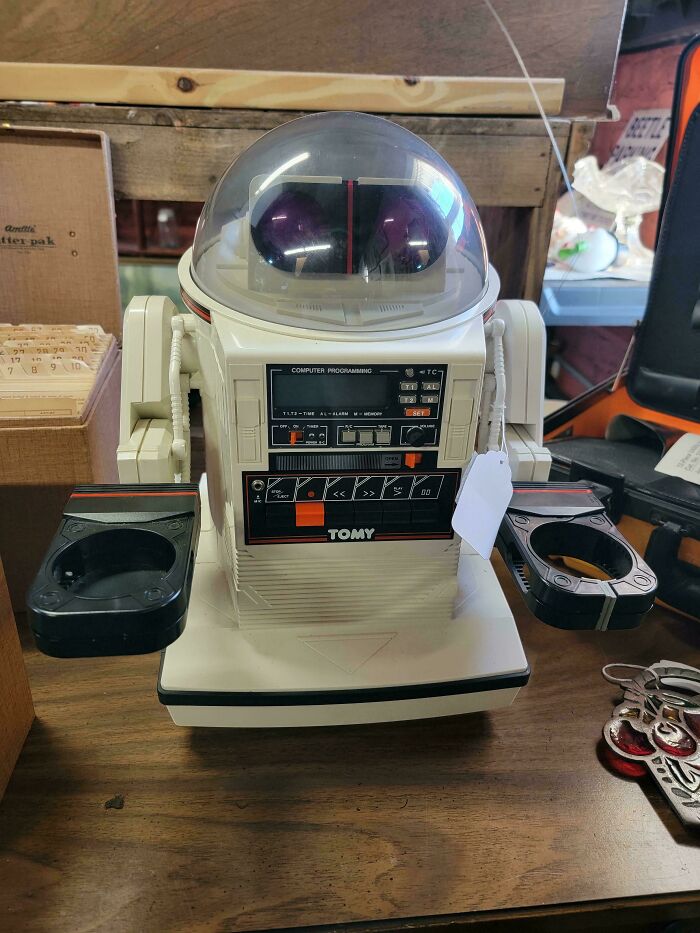 Vintage toy robot with a dome head sitting on a wooden table, featuring control buttons and a display panel.
