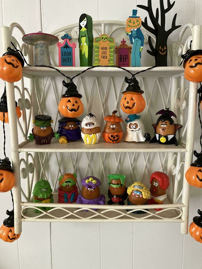 Vintage toys displayed on a shelf with Halloween decorations, featuring pumpkin lights and retro figurines.