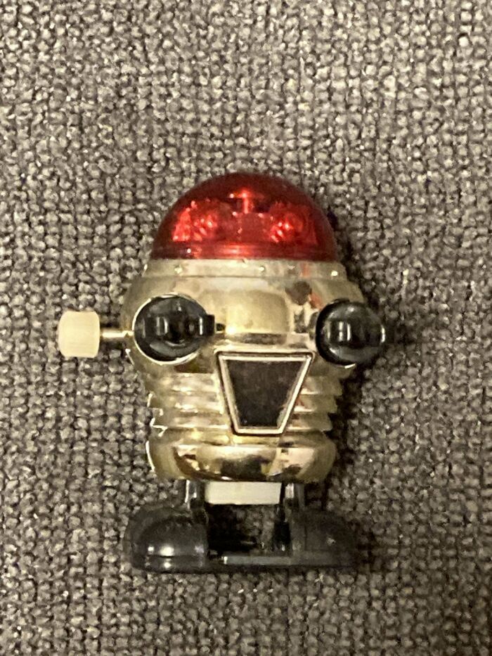 Vintage toy robot with a red dome and metallic body on a textured surface.