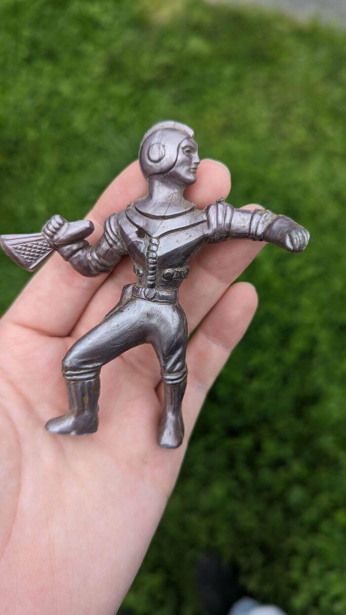 A hand holds a vintage toy spaceman with a helmet, set against a green background.