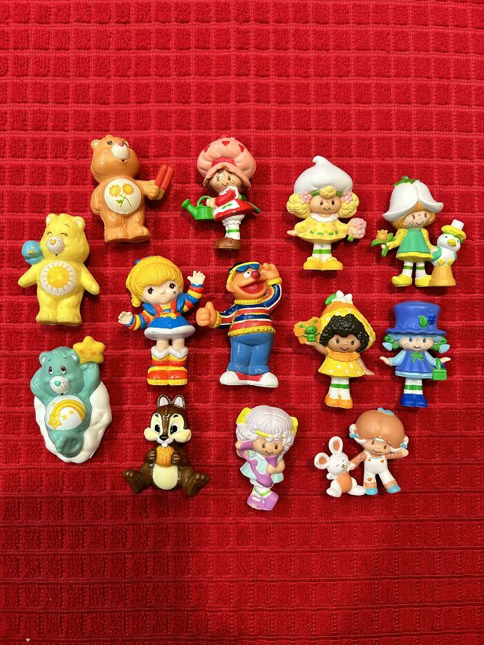 Vintage toys assortment on red background, featuring colorful figures of bears, children, and animals.