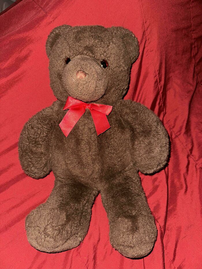 Vintage toy teddy bear with a red bow, sitting on a red fabric background.