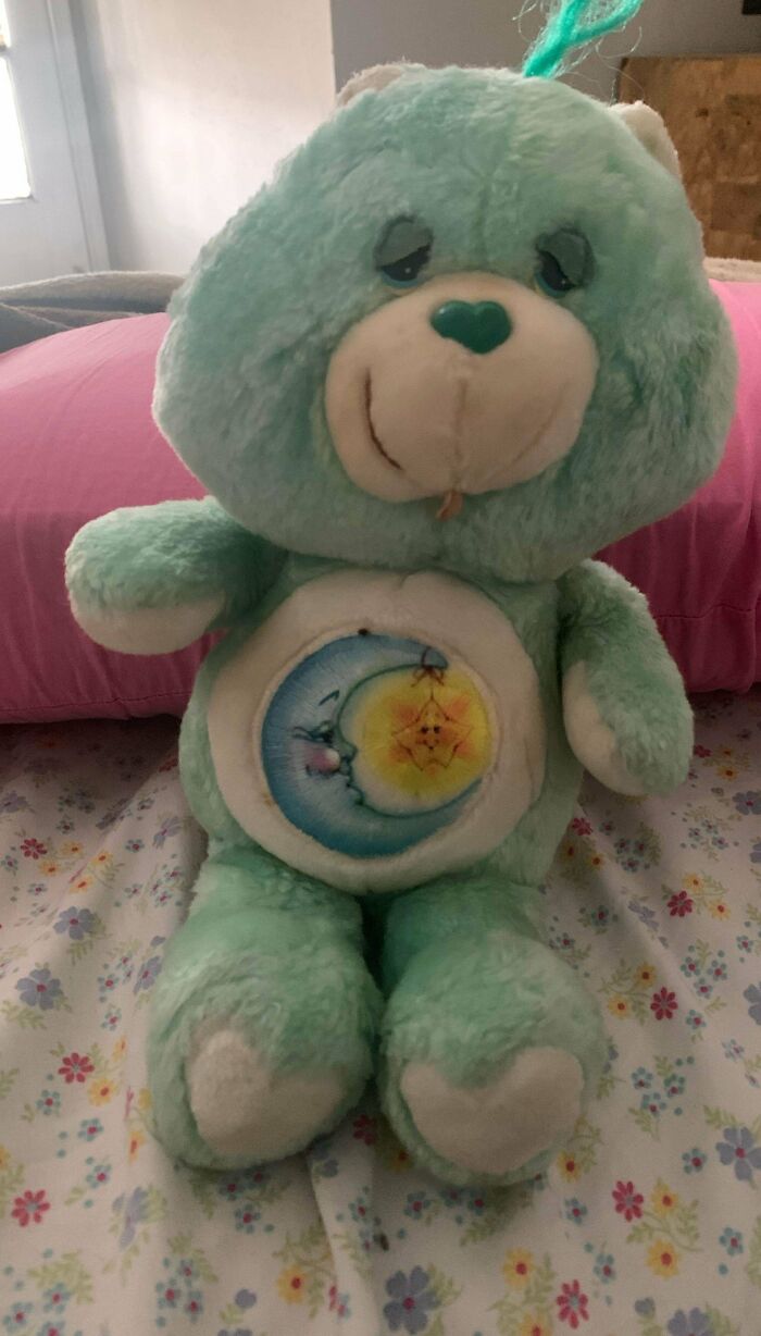 Vintage stuffed bear toy with a moon and star design on its belly, placed on a floral bedspread.