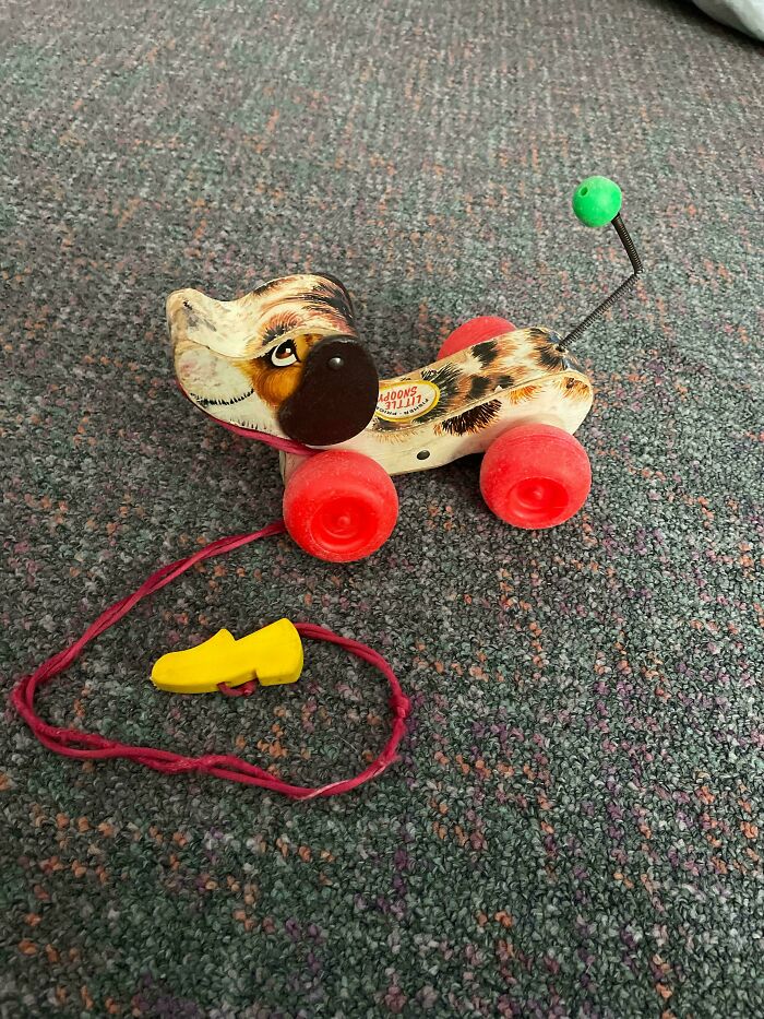 Vintage toy dog on wheels with a pull string and a yellow handle on a carpet.