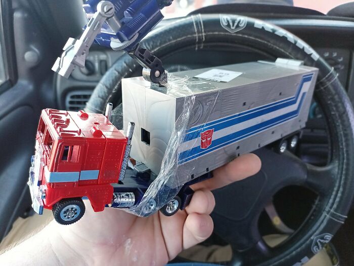 Vintage toy truck and trailer being held in hand inside a car, featuring a robot arm on top.