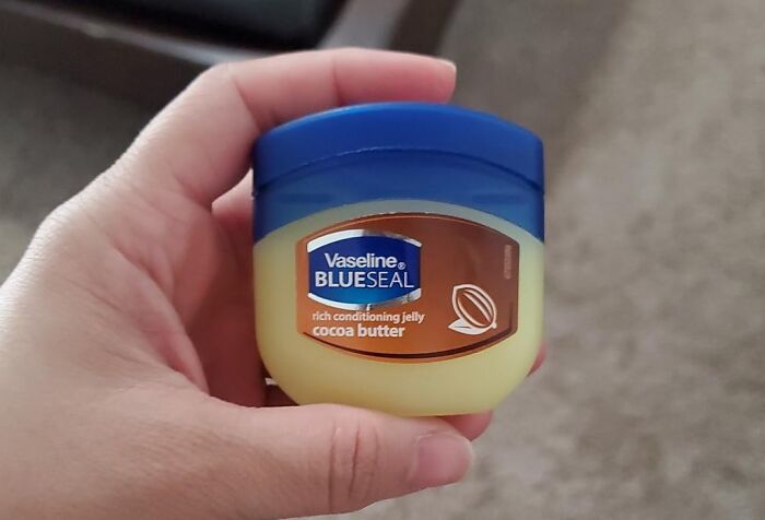 Hand holding a jar of Vaseline Blue Seal, rich conditioning jelly, showcasing old school beauty hacks.
