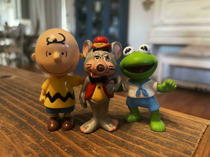 Vintage toys featuring a cartoon boy, a dapper mouse, and a green frog with a sailor outfit on a wooden surface.
