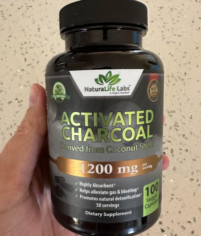 Bottle of activated charcoal, an old school beauty hack, in hand on a speckled surface background.