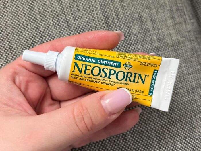 A hand holding a tube of Neosporin, an old school beauty hack for skincare.