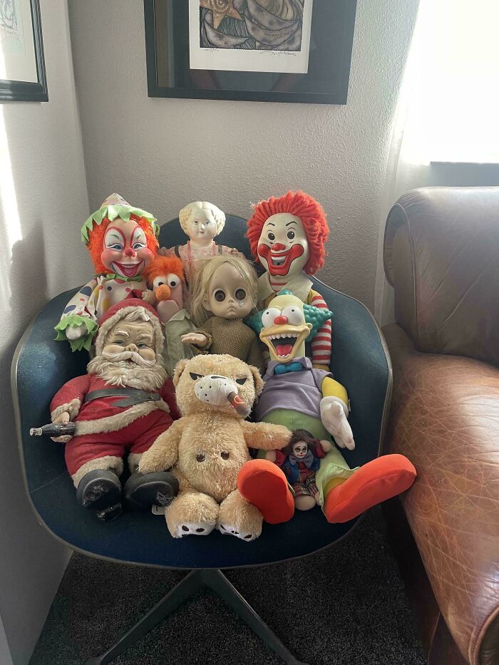 Vintage toys collection on a chair, featuring clowns, dolls, and stuffed animals, evoking childhood nostalgia.
