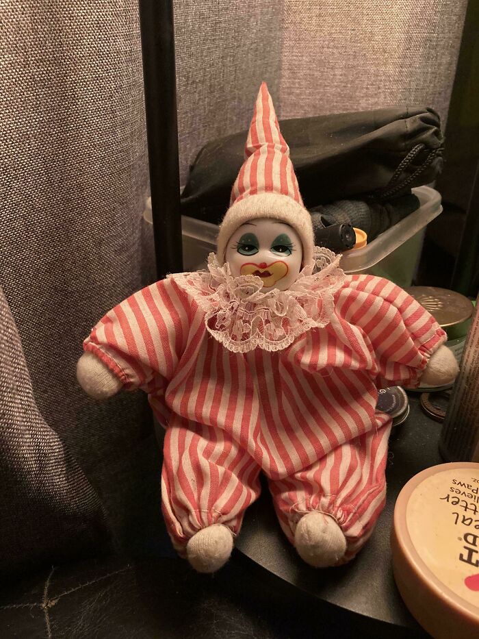 Vintage toy clown doll in pink and white stripes, with a ruffled collar, sitting on a shelf.