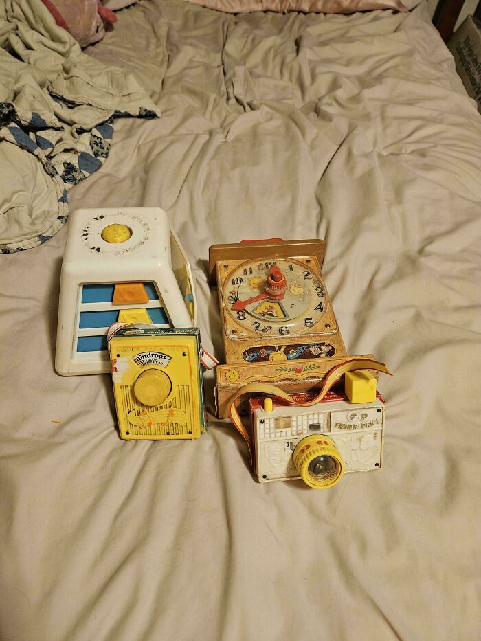 Vintage toys, including a pretend camera and clock, placed on a bed.