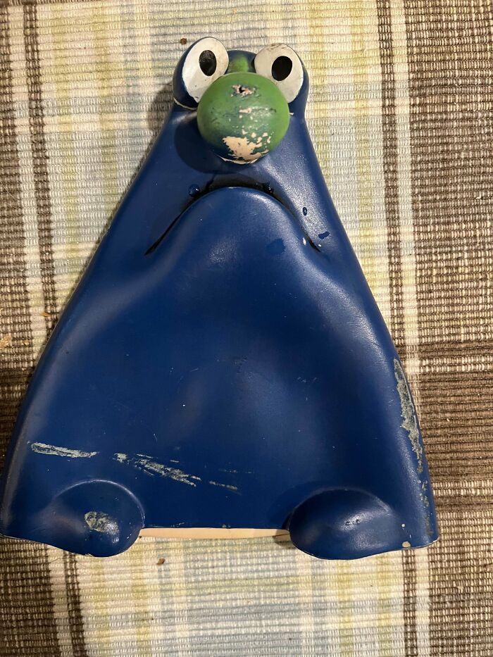 Blue vintage toy resembling a character with a green nose and wide eyes, placed on a checkered background.