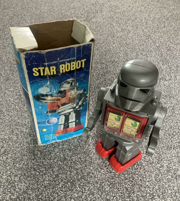 Vintage toy robot with original "Star Robot" box on gray carpet.