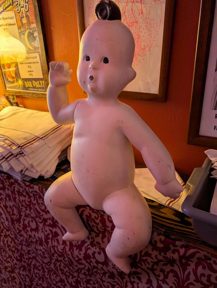 Vintage toy baby doll with an antique finish sitting on a patterned surface in a nostalgic setting.