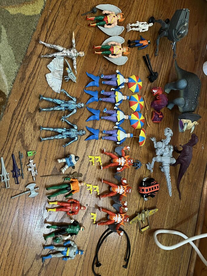 Vintage toys arranged on a wooden floor, including action figures and dinosaurs.