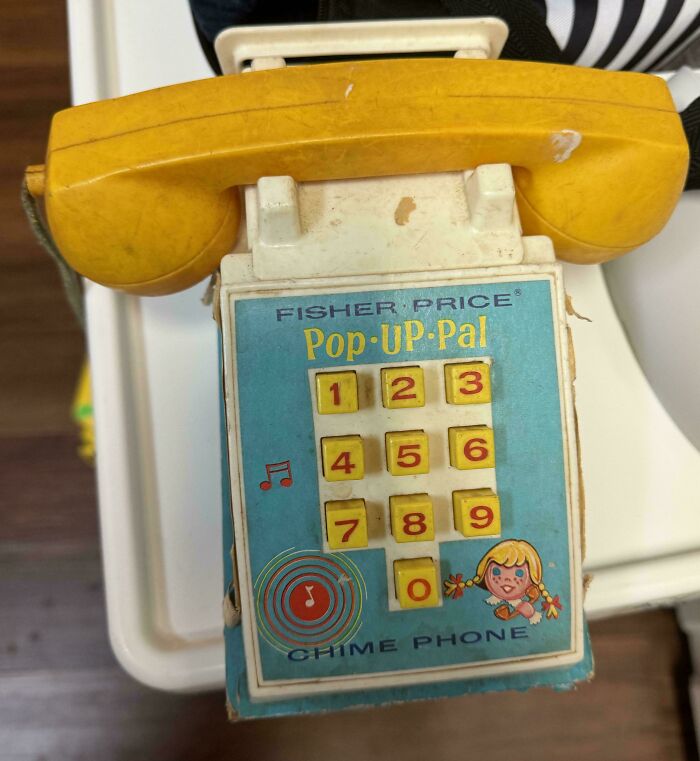 Vintage Fisher Price toy phone with yellow receiver and colorful keypad, evoking childhood nostalgia.