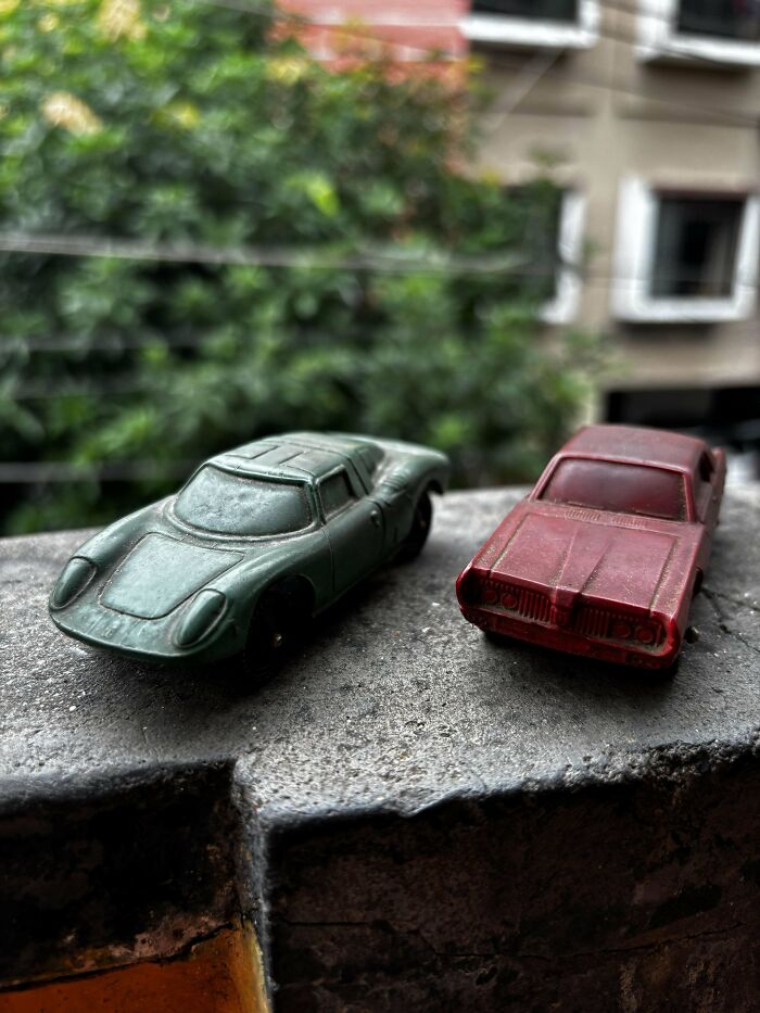 Vintage toys: worn green and red toy cars on a stone ledge with a blurred leafy background.