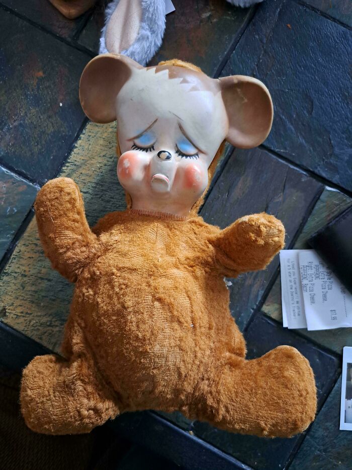 Vintage toy bear with a ceramic face and plush body lying on a tiled floor.