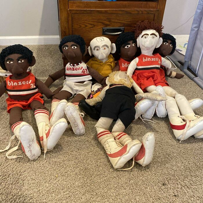 Vintage toys, including retro dolls in sports uniforms, arranged in front of a wooden cabinet on a carpeted floor.