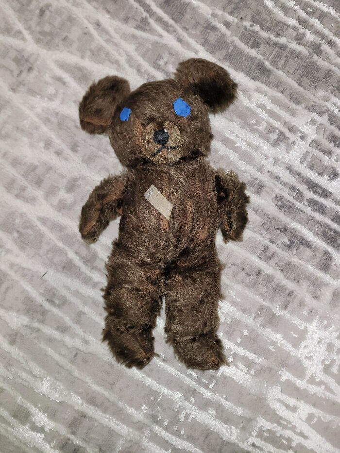 Vintage toy, a well-loved brown teddy bear with blue eyes, lying on a patterned surface.