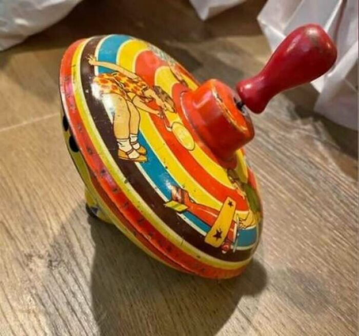 Colorful vintage toy spinning top with red handle on a wooden surface.