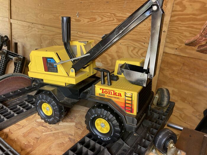 Vintage toy truck with a yellow Tonka design and an excavator arm, displayed in a wooden shed.