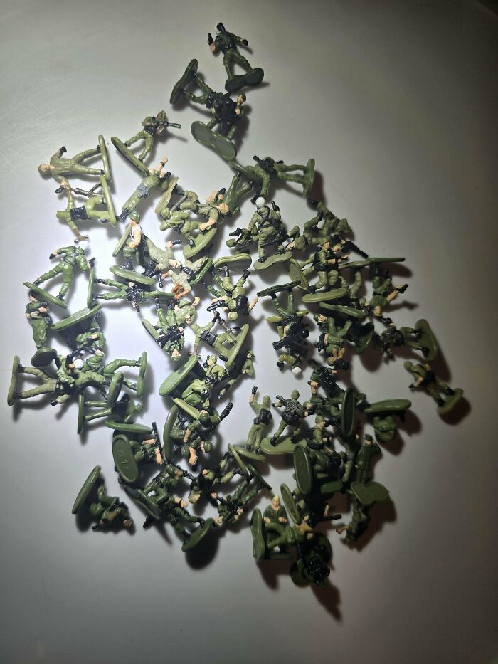 Vintage toys featuring green plastic army men scattered on a white surface.