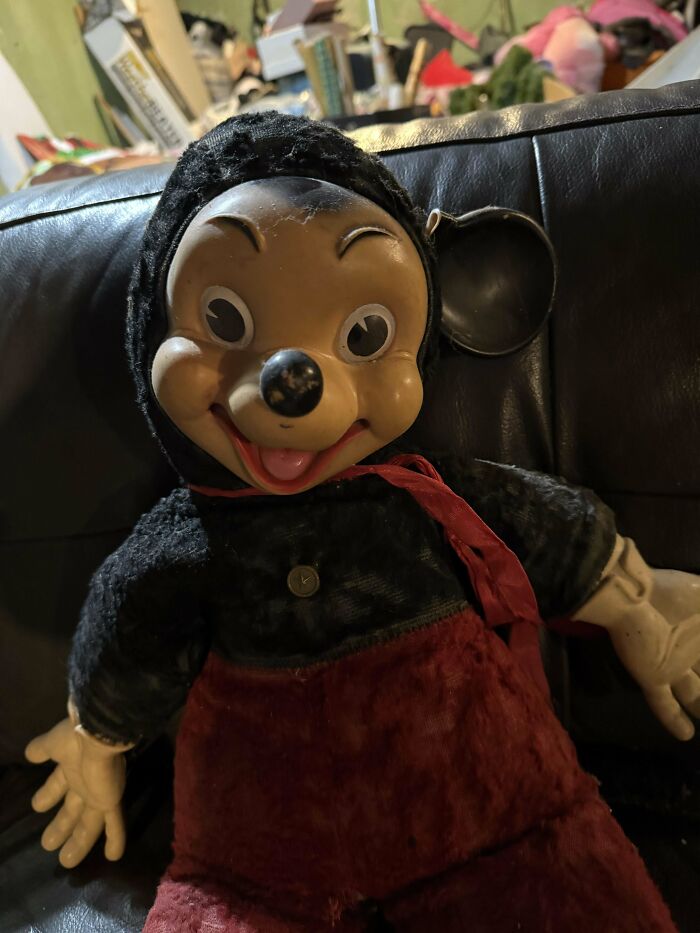 Vintage toy mouse doll with red pants and a black top, sitting on a leather couch, evoking childhood memories.