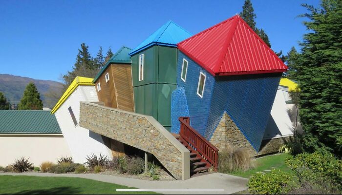 Colorful upside-down house in a lush garden, showcasing a unique tourist experience.