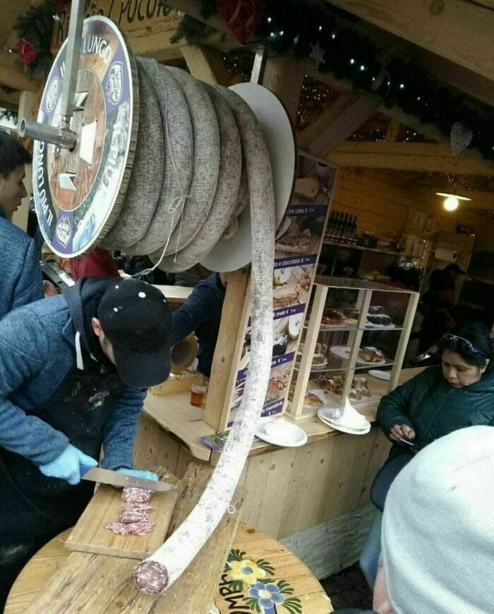 Man slicing a long salami from a large spool at a market, showcasing a tourist-interesting experience.