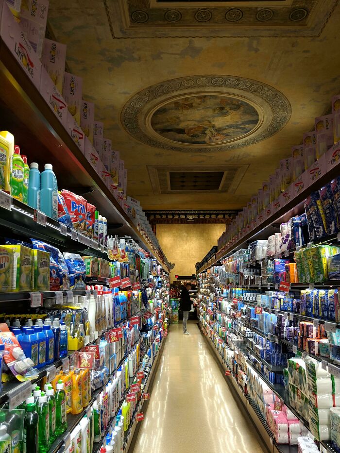 A decorated supermarket ceiling provides a unique tourist experience with ornate artwork amidst grocery aisles.