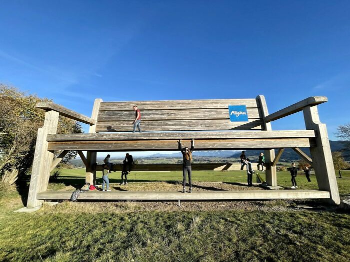 Giant bench in a field with people interacting, offering unique tourist experiences under a clear blue sky.