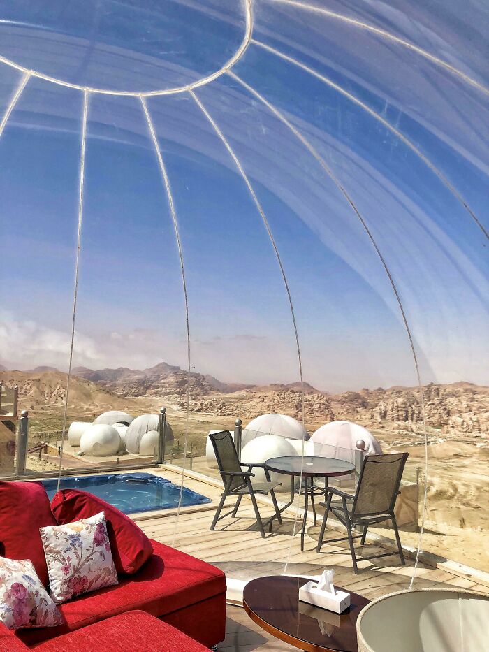 Transparent dome room with red sofa overlooking desert mountains, offering unique tourist experiences.