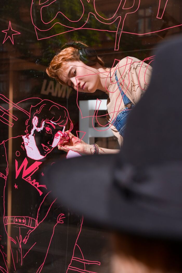 Artist drawing on glass in Oslo street, wearing headphones, captures essence of city life.