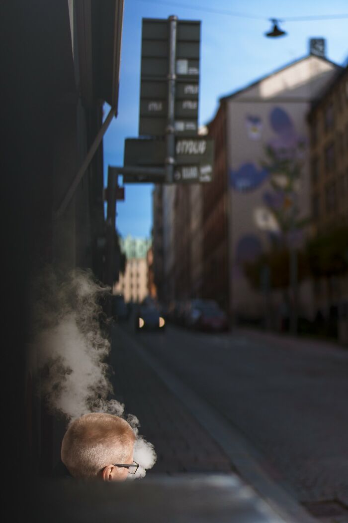 Man exhaling vapor in Oslo street, capturing essence of city life with a blurred urban background.
